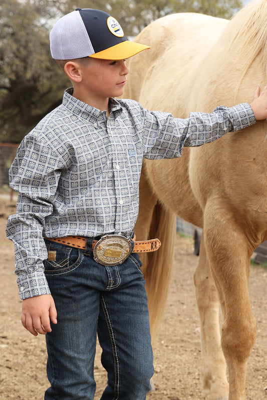 Boy wearing a white and navy Cinch shirt, blue jeans and  ball cap petting a horse