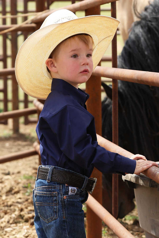 Child wearing a cowboy hat and navy blue cinch shirt next to a horse.