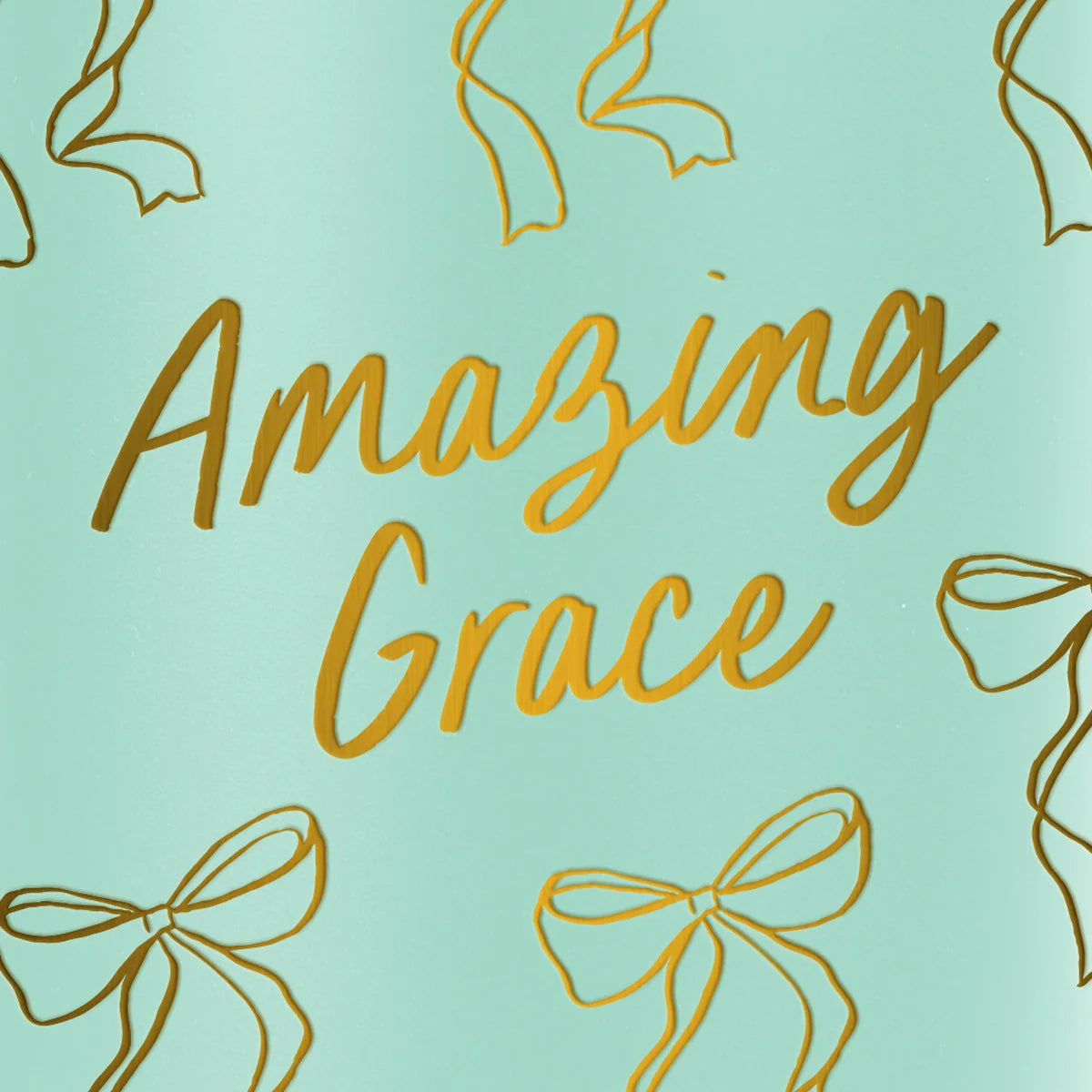 A close-up of a mint green mug from Kerusso with metallic gold foil text reading 'Amazing Grace' and gold ribbon line drawings around it.