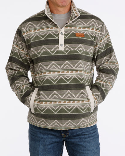 Man wearing an olive Cinch fleece pullover and blue jeans on a white background