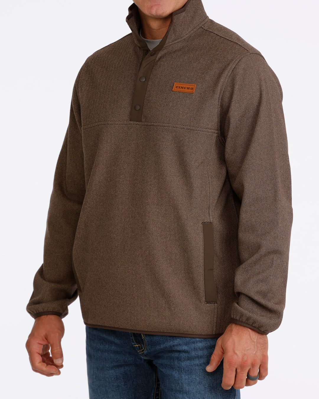 Man wearing a brown Cinch pullover sweater and blue jeans on a grey background