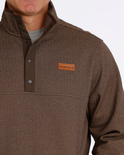 Close up of a man wearing a brown pullover sweater by Cinch on a grey background