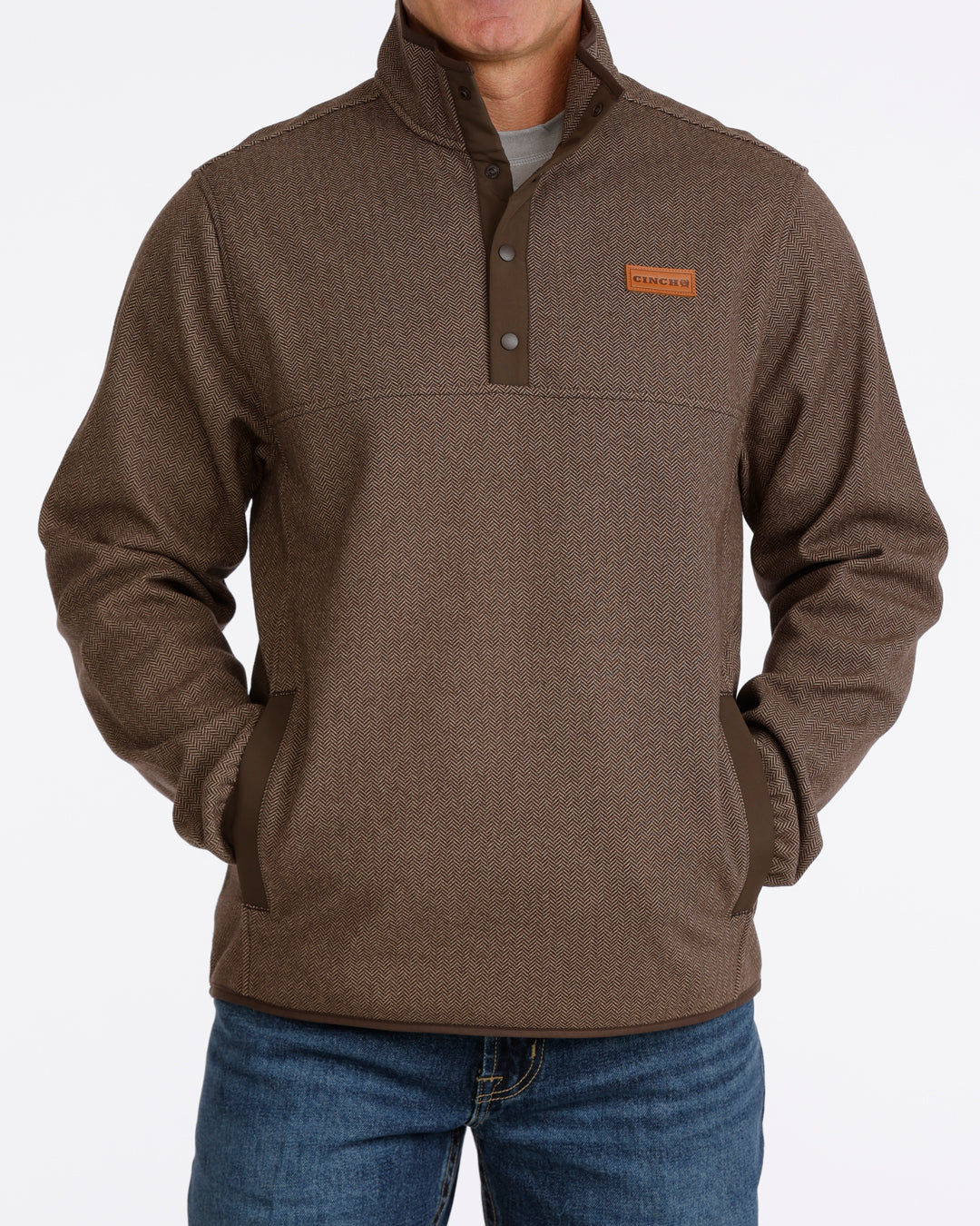 Man wearing a brown Cinch pullover sweater and blue jeans on a grey background