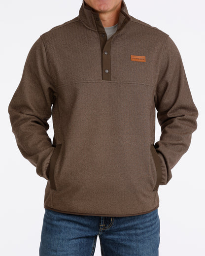 Man wearing a brown Cinch pullover sweater and blue jeans on a grey background