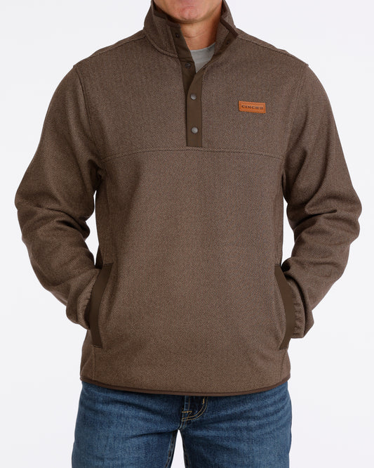 Man wearing a brown Cinch pullover sweater and blue jeans on a grey background