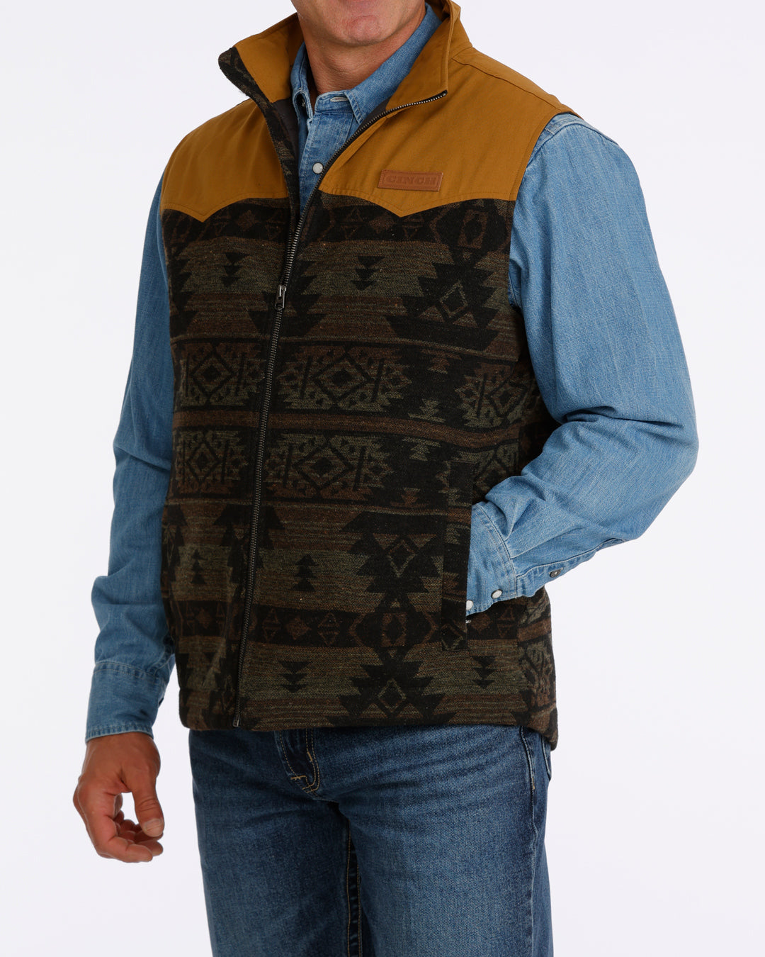 man wearing a Cinch vest with aztec design, denim shirt and blue jeans on a white background