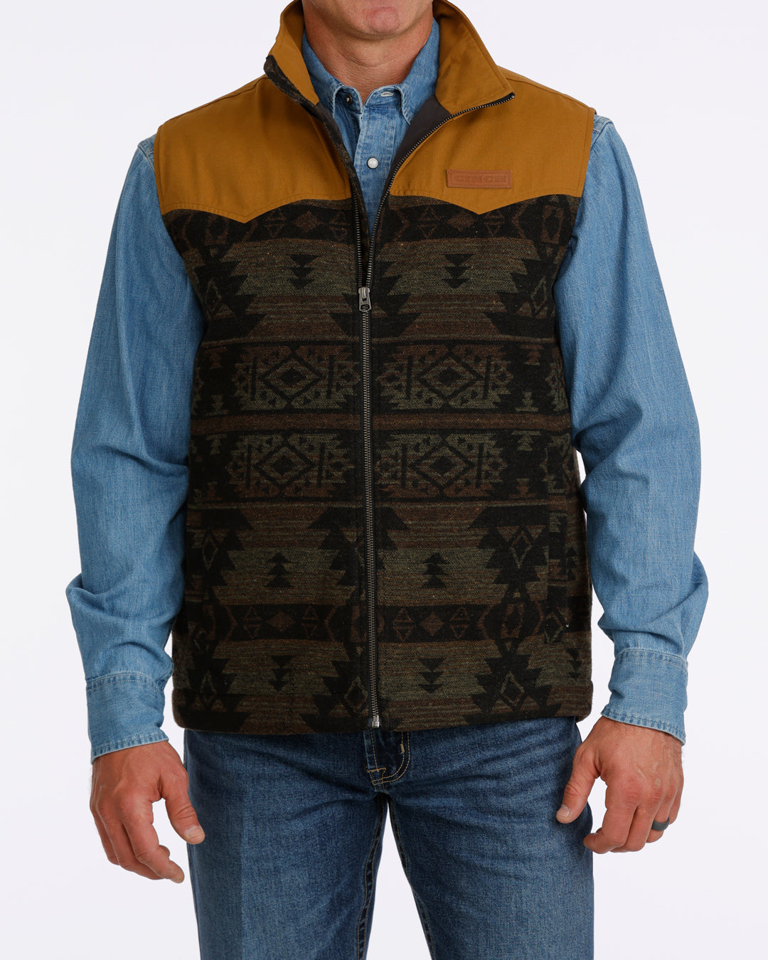 man wearing a Cinch vest with aztec design, denim shirt and blue jeans on a white background