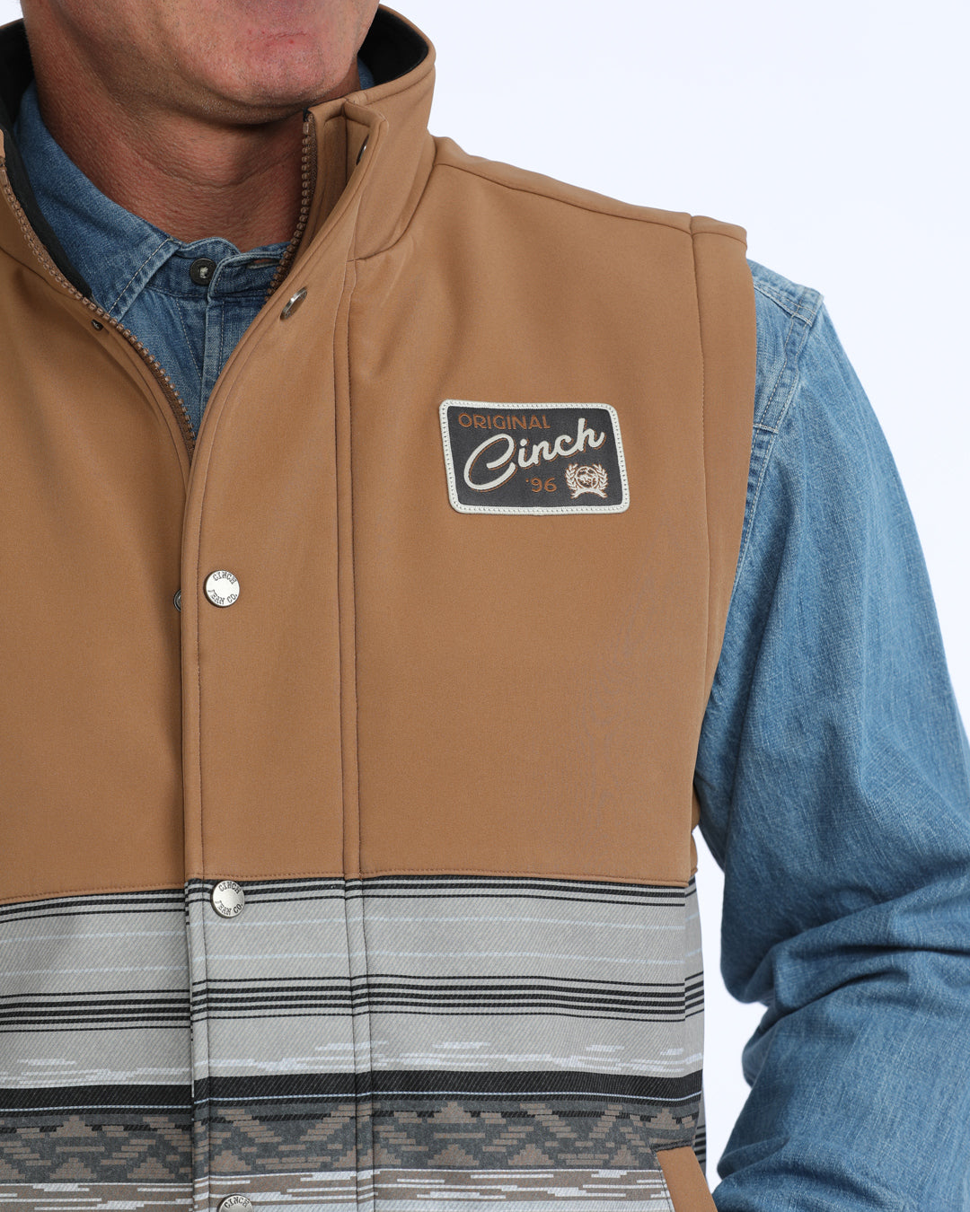 Man wearing a tan and grey Cinch vest with a denim shirt on a white background
