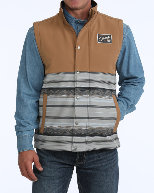 Man wearing a tan and grey Cinch vest with a denim shirt and blue jeans on a white background