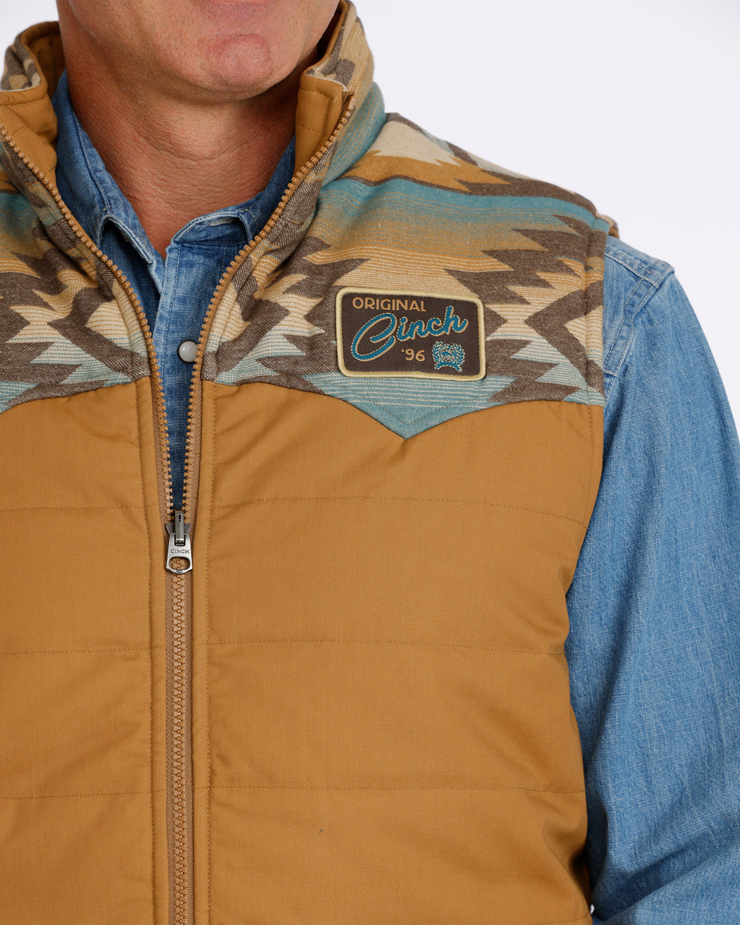 man wearing a tan Cinch vest with bue aztec design and a denim shirt on a white background