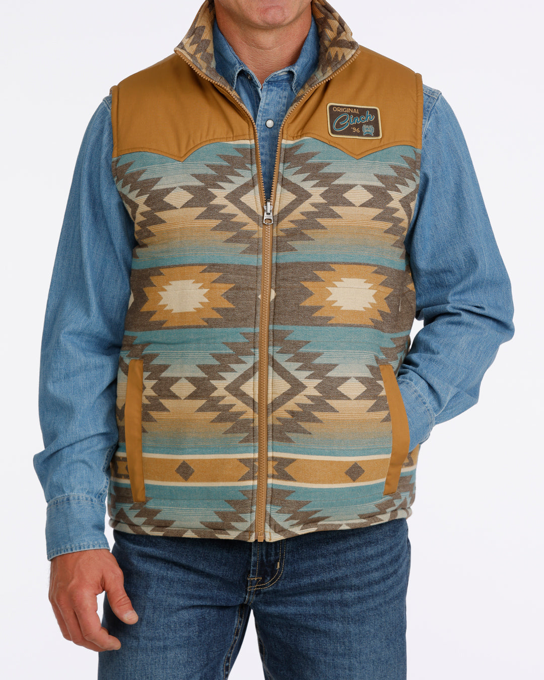 man wearing a tan Cinch vest with bue aztec design, denim shirt and blue jeans on a white background