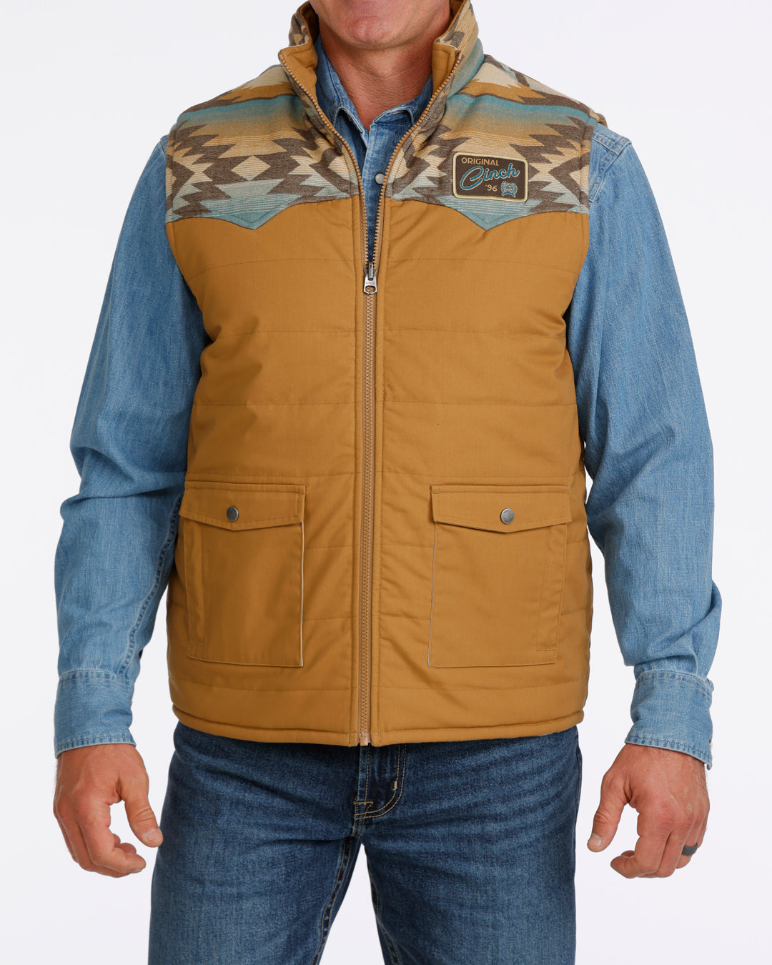 man wearing a tan Cinch vest with bue aztec design, denim shirt and blue jeans on a white background
