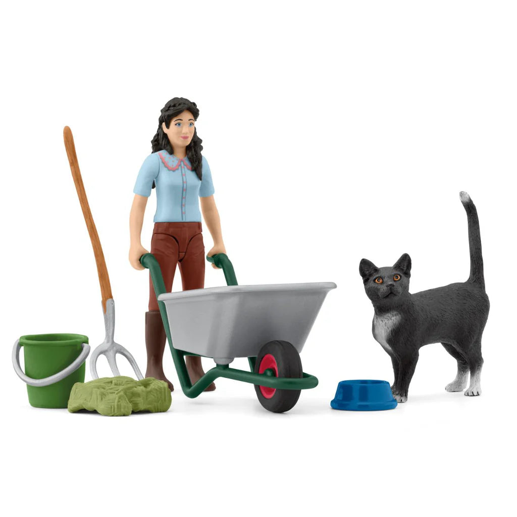 Schleich toy figurine of a woman with a wheelbarrow, gardening tools, and a cat on a white background