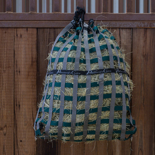 Professional's Choice Hay net with green and gray straps hanging against a wooden fence