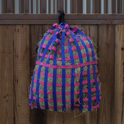 Professional's choice Hay bag with pink and blue straps hanging on a wooden fence