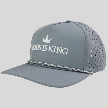 A gray baseball cap from Kerusso  with white embroidered text reading 'JESUS IS KING' and a small crown above it, plus a silver chain detail across the brim, shown on a light gray background.
