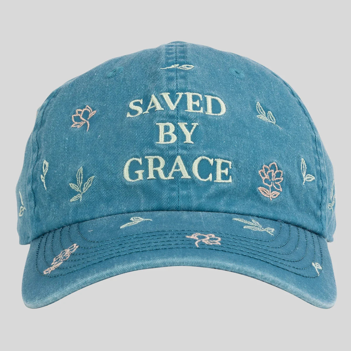 A blue distressed baseball cap from Kerusso with 'SAVED BY GRACE' embroidered in cream on the front, surrounded by small floral and leaf motifs, shown against a light gray background.
