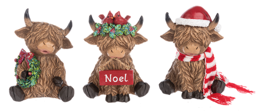 Three Highland cow Christmas figurines from Ganz on a white background. The left cow holds a green wreath with a red bow.