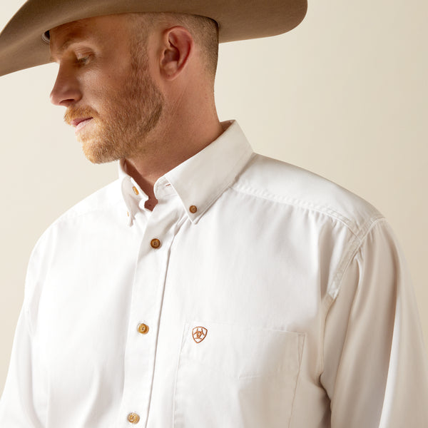 Man wearing a beige cowboy hat and white Ariat shirt with a brand logo on a plain background