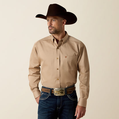 Man wearing a beige Ariat shirt, dark jeans, and a brown cowboy hat on a beige background