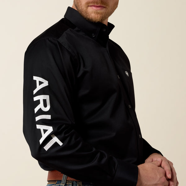 Man wearing a black jacket with 'Ariat' branding on a beige background
