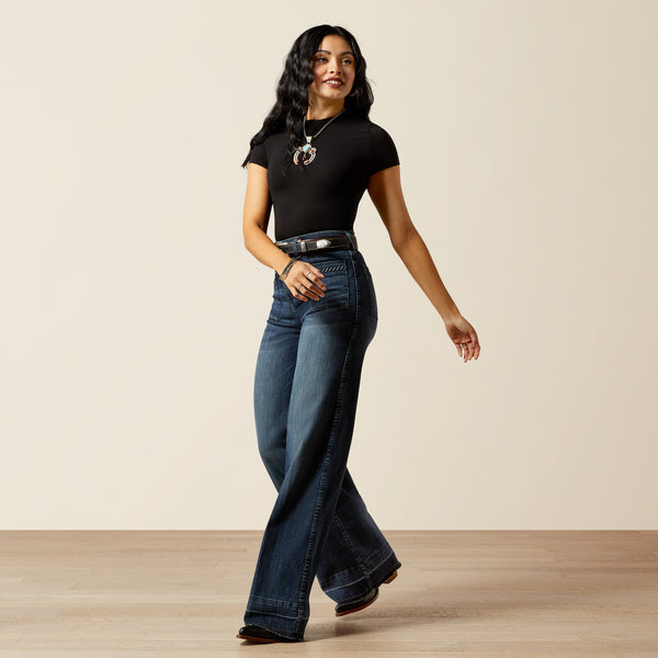 woman wearing blue Ariat jeans, a black t shirt and cowboy boots on a cream background