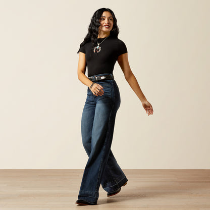 woman wearing blue Ariat jeans, a black t shirt and cowboy boots on a cream background