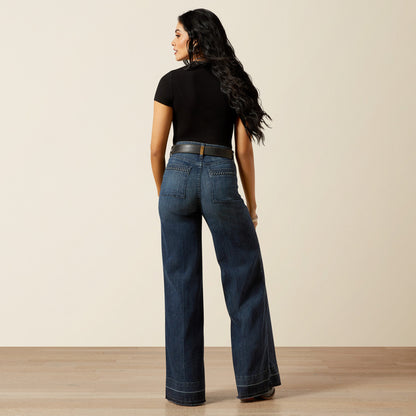 woman wearing blue Ariat jeans, a black t shirt and cowboy boots on a cream background