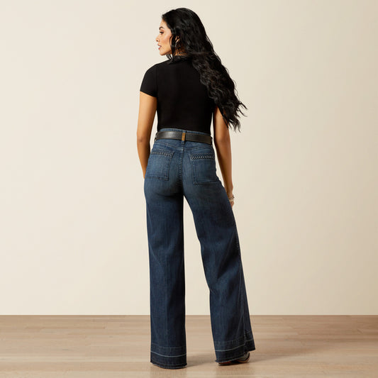 woman wearing blue Ariat jeans, a black t shirt and cowboy boots on a cream background
