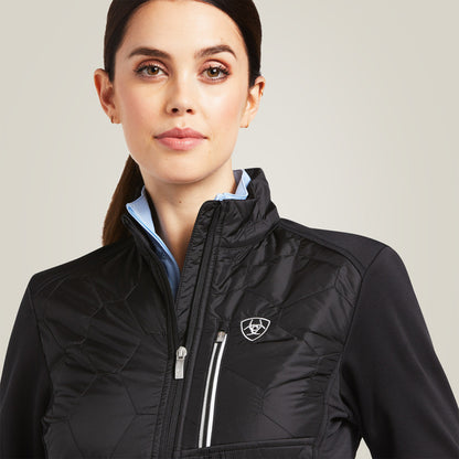 Woman wearing a black jacket with a visible Ariat logo on a light gray background