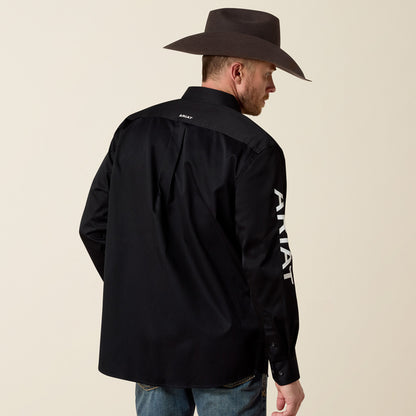 Man wearing a black Ariat shirt with branding on the back and side, standing against a beige background