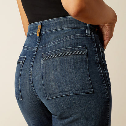 woman wearing blue Ariat jeans, and a black t shirt on a cream background