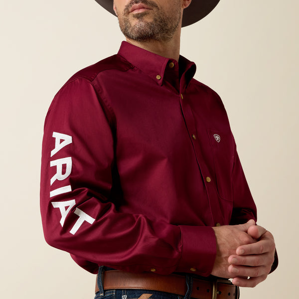 Man wearing a maroon Ariat shirt with branding on a beige background