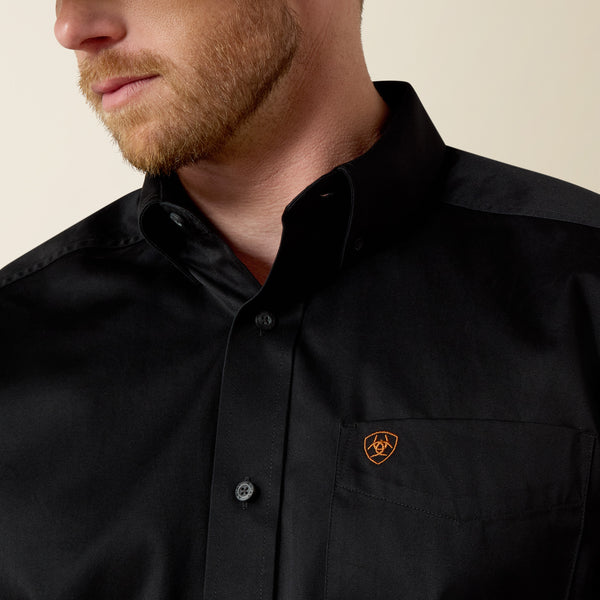 Close-up of a person wearing a black Ariat shirt with a logo on the chest against a beige background