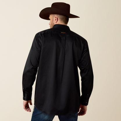 Man wearing a black Ariat shirt and brown cowboy hat on a beige background