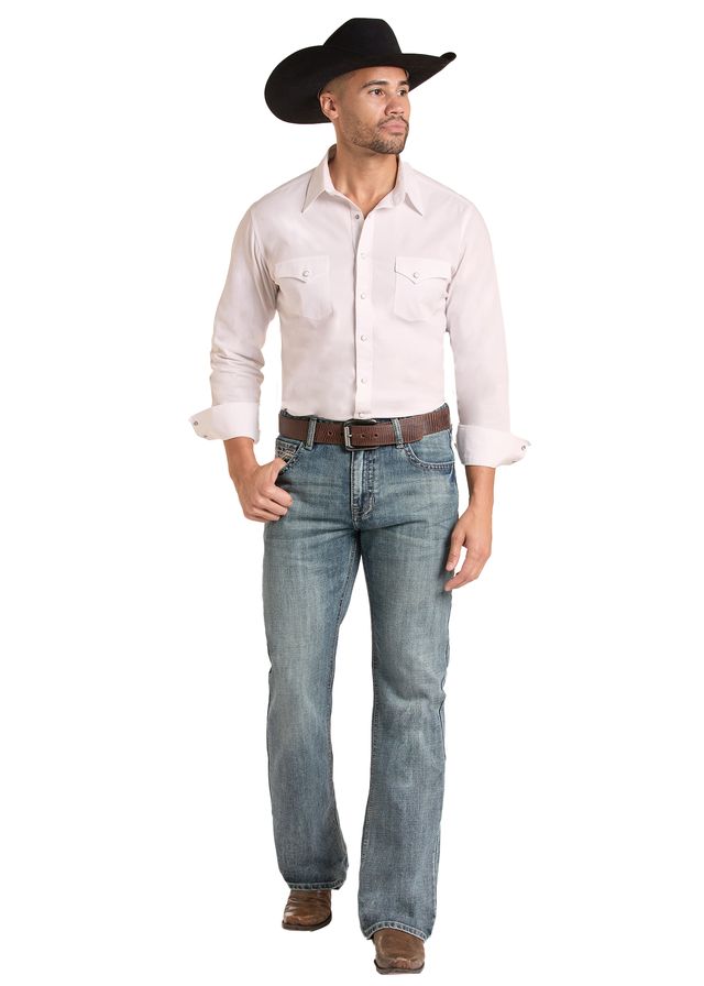 A man wearing a light pink western-style shirt, blue Rock & Roll Denim  jeans, a brown belt, and a black cowboy hat, against a plain white background.