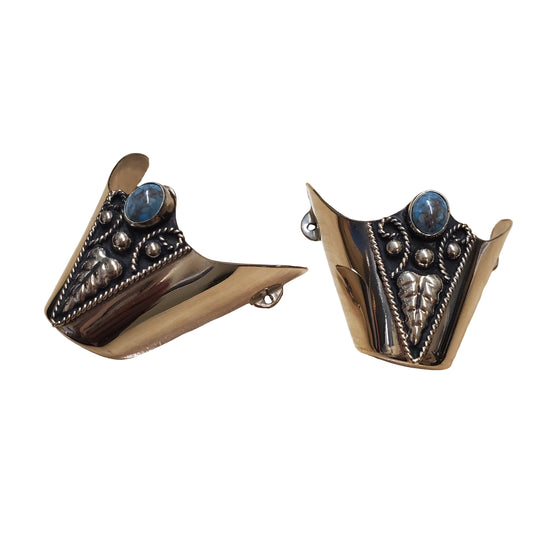 A pair of silver-toned metal cuff-style earrings with blue oval stones and ornate engraved details