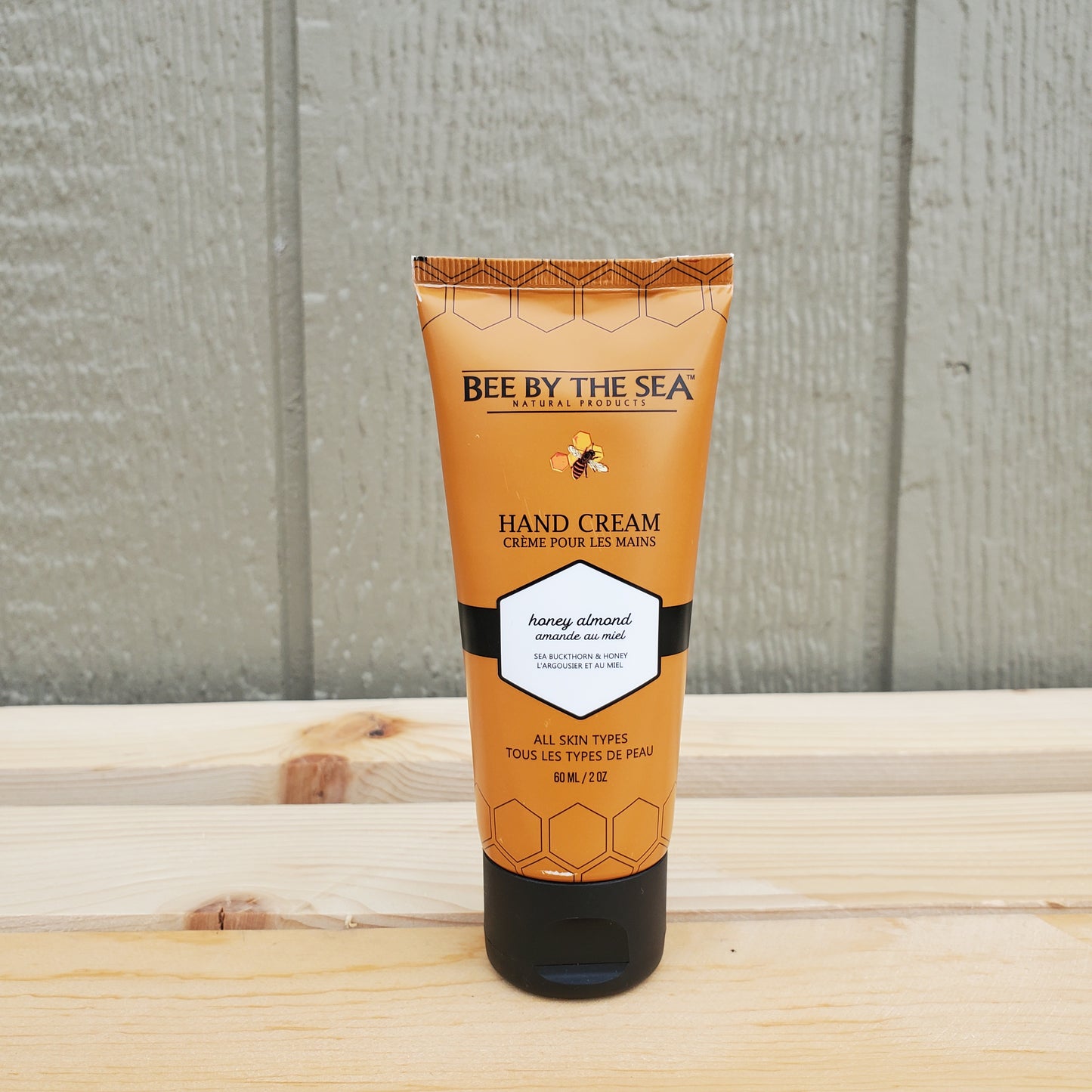 Hand cream tube labeled 'Bee by the Sea' on a wooden surface.