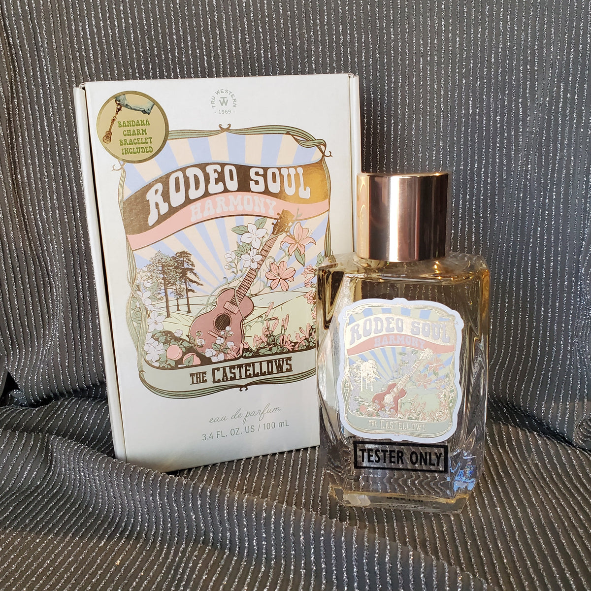 a white box that says Rodeo Soul Harmony The Castellos with a glass bottle of perfume in front of it on a olive colored sparkly background