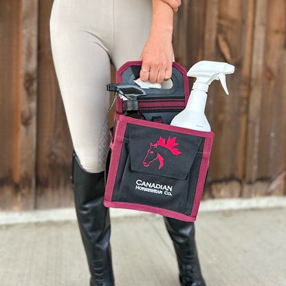 a girl in english riding clothes holding a black and burgundy grooming tote bag in a barn setting