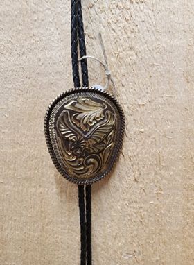 A bolo tie with a brown eagle design against a wooden background.