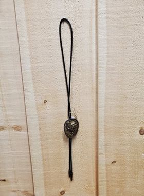 A bolo tie with a brown eagle design against a wooden background.