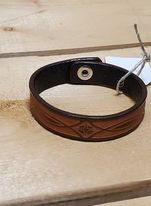 A brown leather bracelet with a stamped pattern, displayed on a wooden surface.