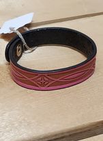 A pink leather bracelet with a stamped pattern, displayed on a wooden surface.
