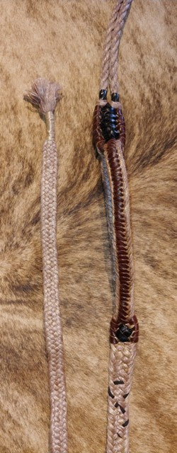 A close-up of a bull rope with a brown handle and lace detailing, displayed on a furry surface.
