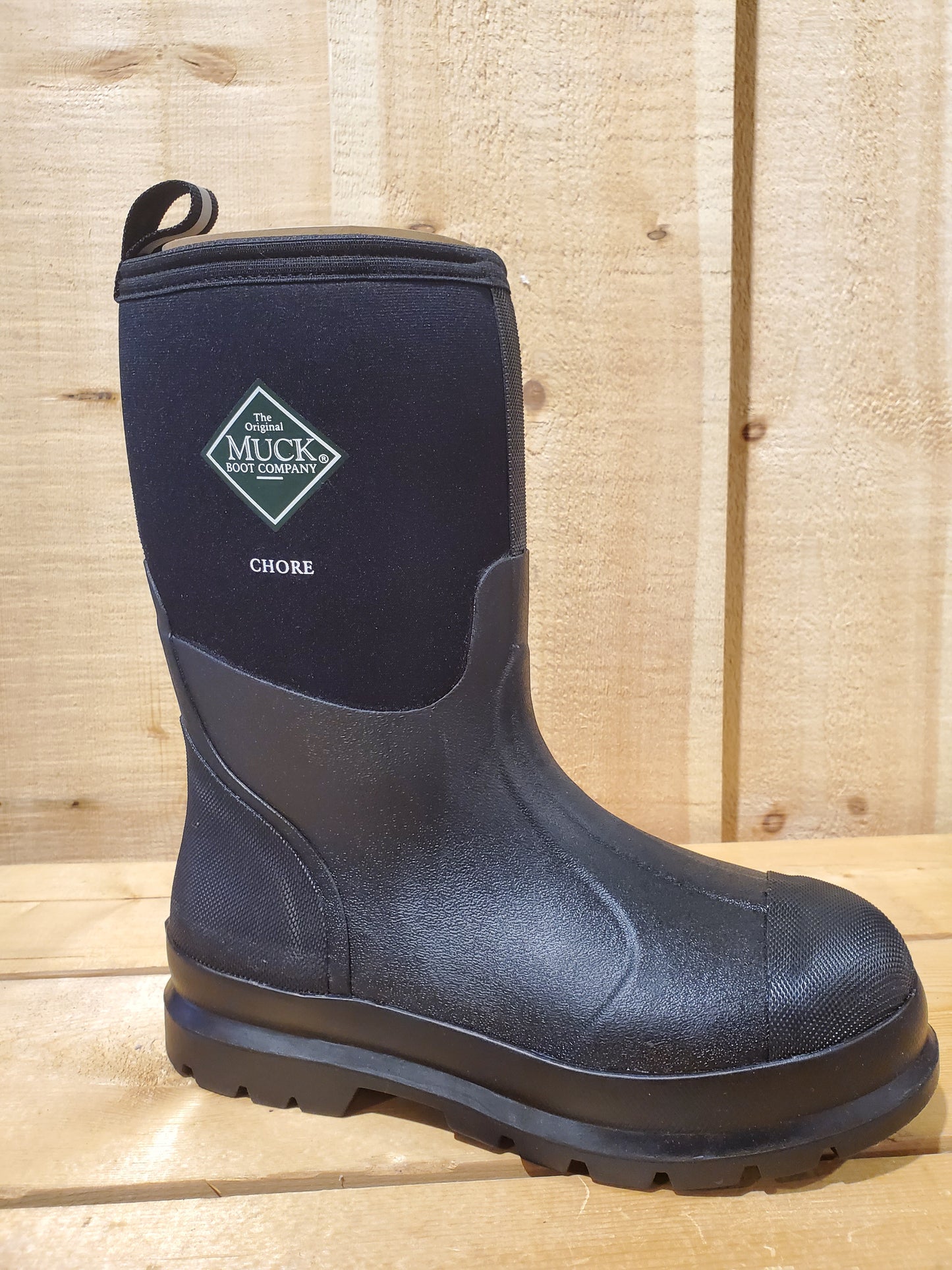 A black mid-height work boot with a label displaying 'MUCK BOOT COMPANY' and the word 'CHORE' on it, featuring a rubber outsole and a breathable Airmesh lining.