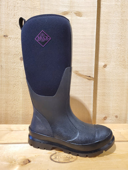 A black 'Chore Tall' women's boot with purple accents, featuring a rubber sole and a breathable arimesh lining, displayed on a wooden surface.
