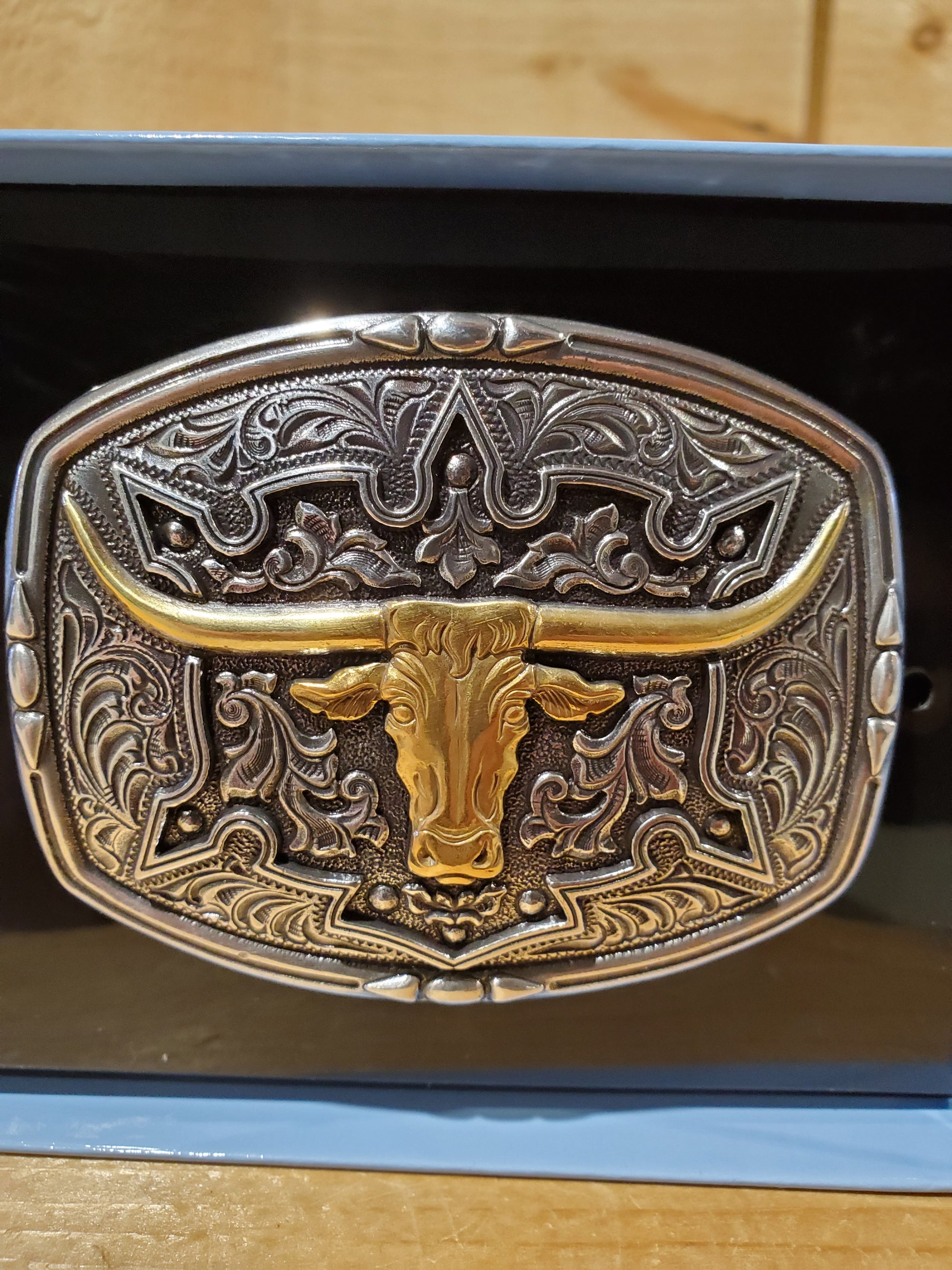 Antique colored belt buckle with a steerhead design, displayed in an open box with a black interior.