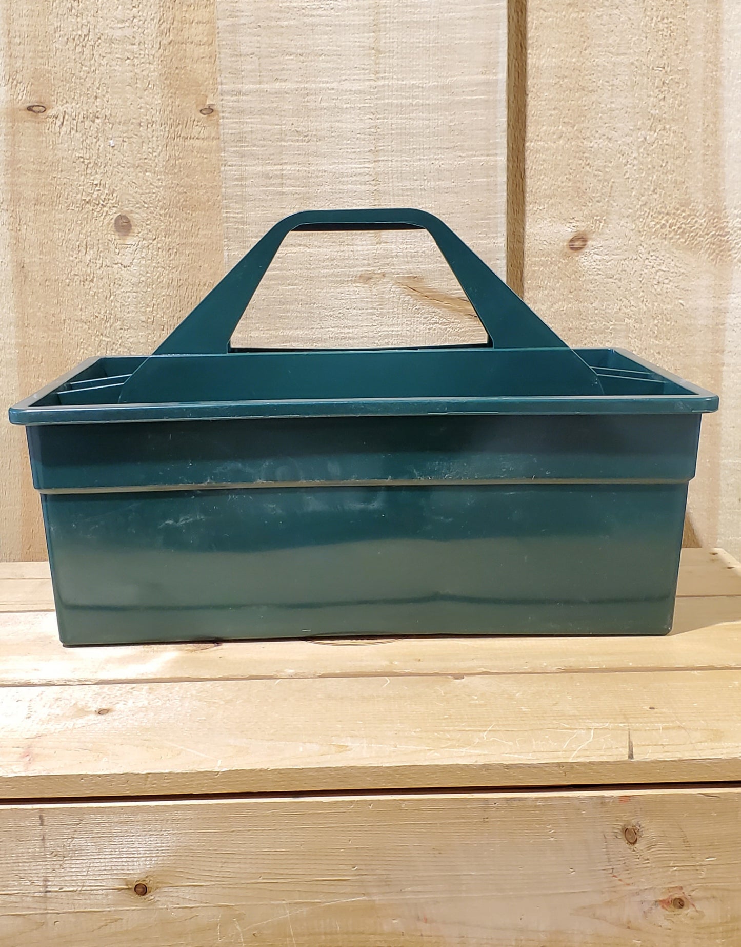 A hunter green plastic utility tote with a handle, designed to be carried by hand and to fit onto a fence board.