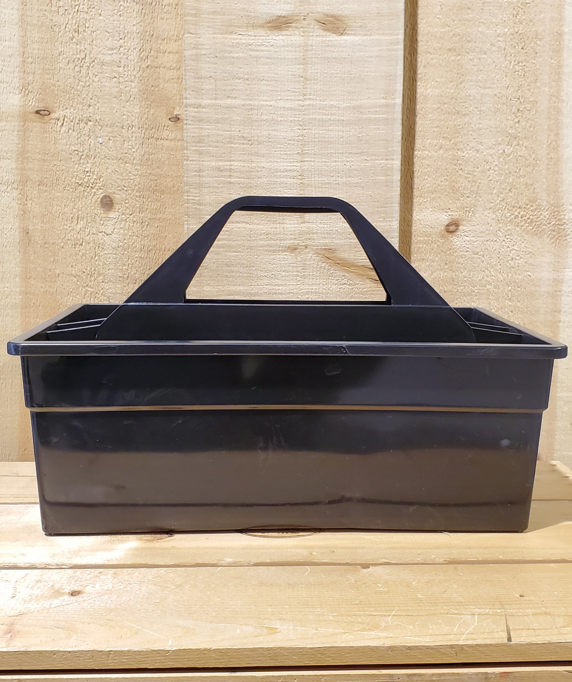 A black plastic utility tote with a handle, designed to be carried by hand and to fit onto a fence board.